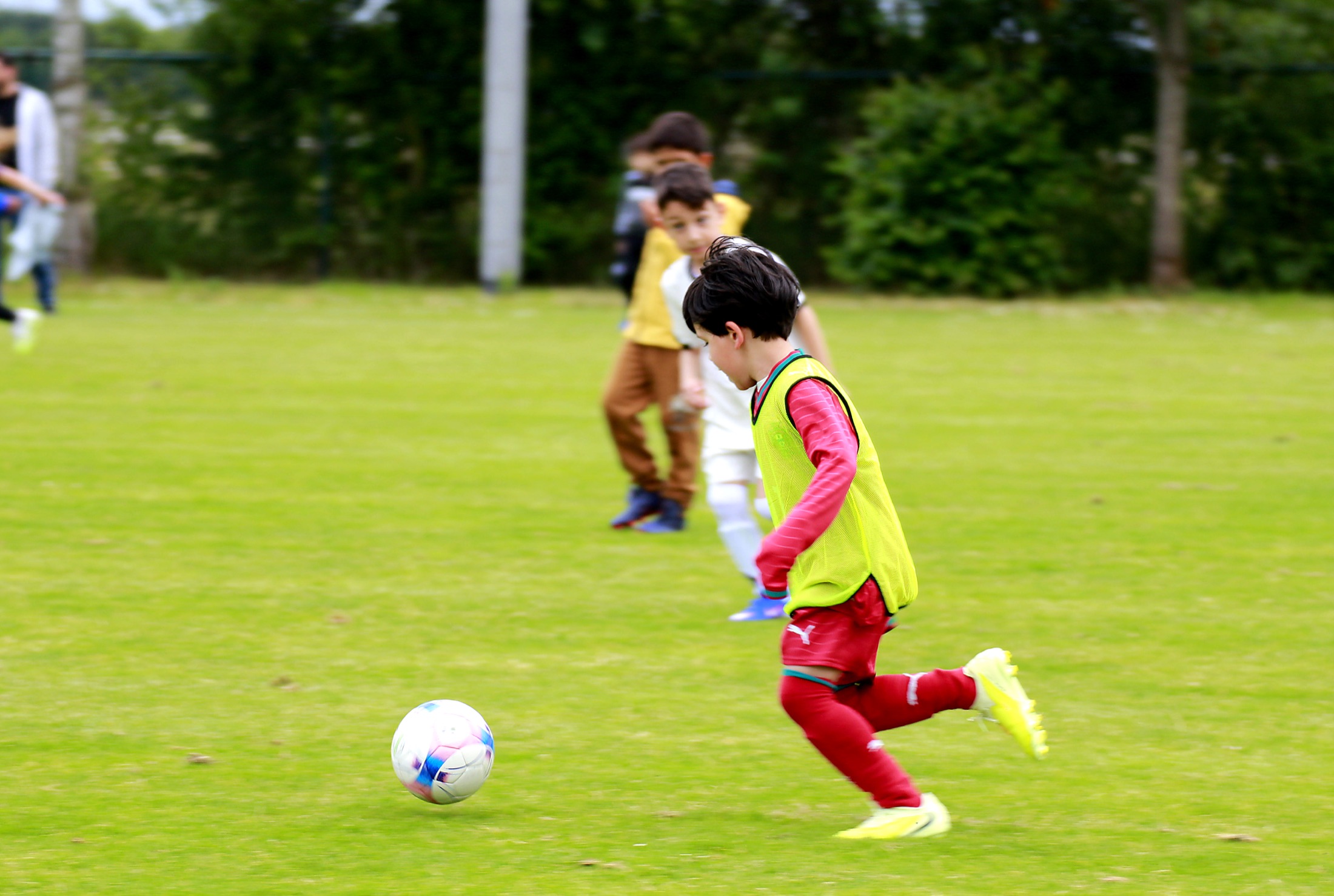 Kind im gelben Leibchen läuft dem Ball entgegen